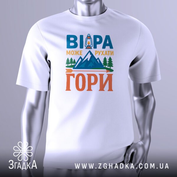 Біла футболка з графічним принтом у центрі. Принт виконаний у темних тонах і зображує гірський пейзаж, можливо, зі сходом або заходом сонця за горами. Над горами великими літерами написано фразу: "ВІРА МОЖЕ РУХАТИ ГОРИ". У нижній частині принта видно стилізовану стрілу, що вказує вгору, і зображення ліхтаря або джерела світла, що символізує шлях. Футболка на сірому манекені.