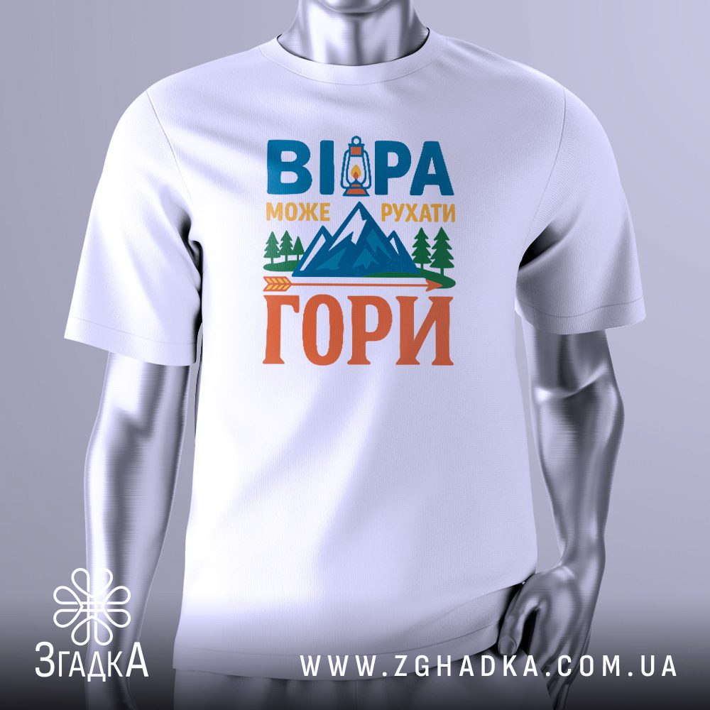 Біла футболка з графічним принтом у центрі. Принт виконаний у темних тонах і зображує гірський пейзаж, можливо, зі сходом або заходом сонця за горами. Над горами великими літерами написано фразу: "ВІРА МОЖЕ РУХАТИ ГОРИ". У нижній частині принта видно стилізовану стрілу, що вказує вгору, і зображення ліхтаря або джерела світла, що символізує шлях. Футболка на сірому манекені.