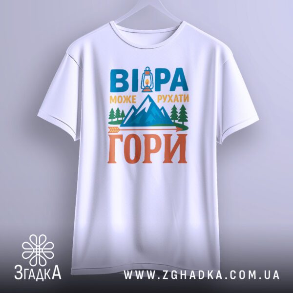 Біла футболка з принтом "рушійна сила віри", що висить на білих плічках, демонструючи дизайн.
