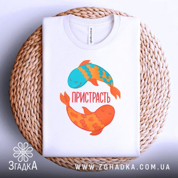 Біла футболка з принтом "пристрасть", акуратно складена на круглому плетеному підносі.