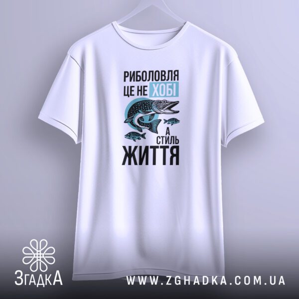 Біла футболка з принтом "Моє хобі – РИБОЛОВЛЯ", що висить на вішаку.