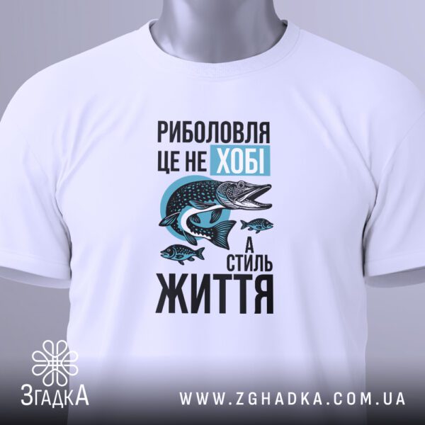 Крупний план кольорового принту чоловіка, що ловить рибу, та напису "Моє хобі – РИБОЛОВЛЯ" на білій футболці.