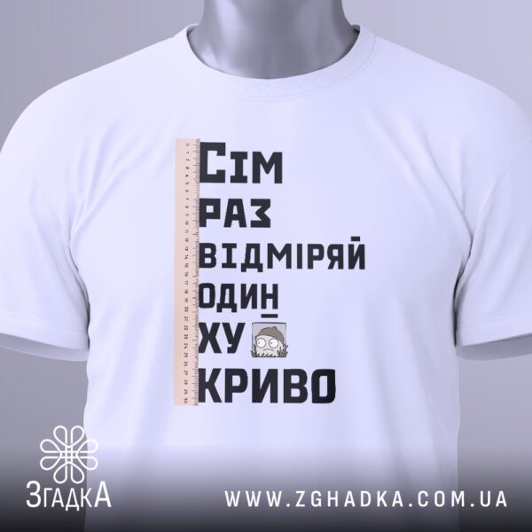 Крупний план принта "сім раз відміряй" на білій футболці, що детально показує лінійку та текст.