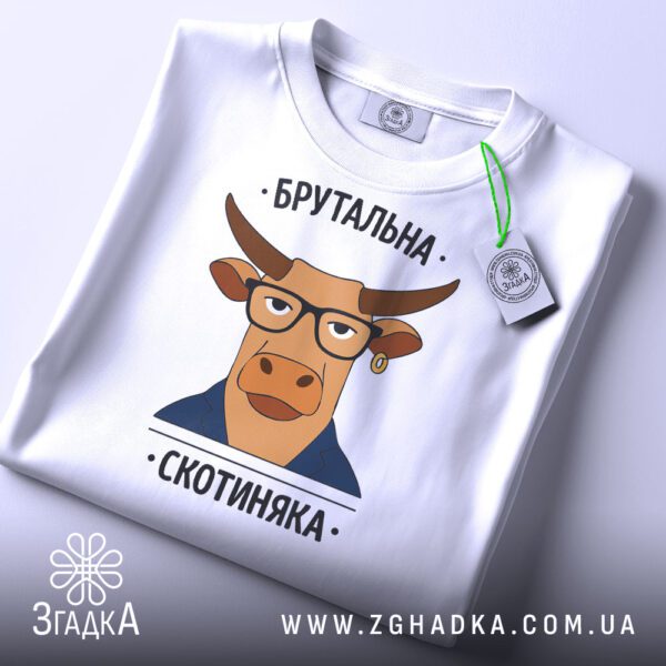 Складена біла футболка з чорним текстовим принтом "Брутальна скотиняка" та етикеткою "Згадка".