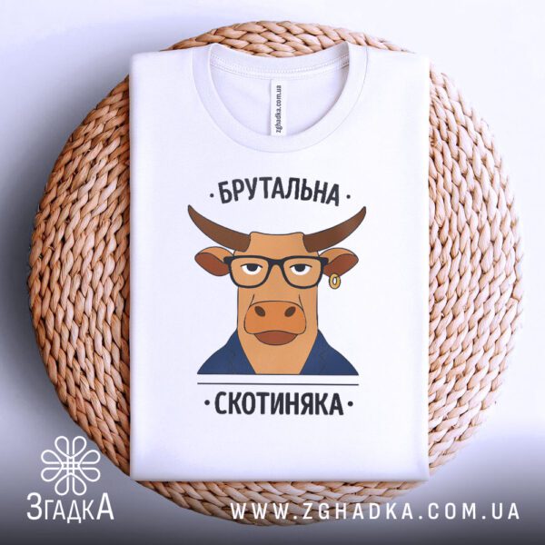 Біла футболка з принтом "Брутальна скотиняка", акуратно складена на круглому плетеному підносі.