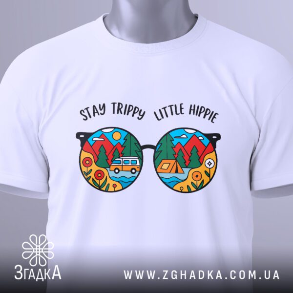 Крупний план принта "Stay trippy little hippie" з кольоровими окулярами та пейзажем на білій футболці, що детально показує графіку та кольори.