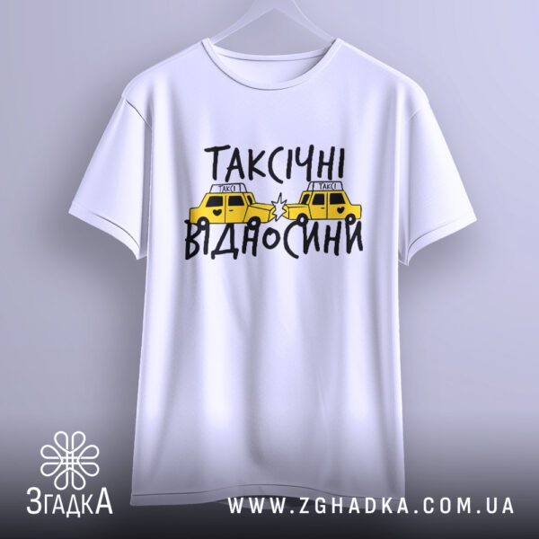 Біла футболка з принтом "таксічні відносини жарт", що висить на білих плічках, демонструючи дизайн.