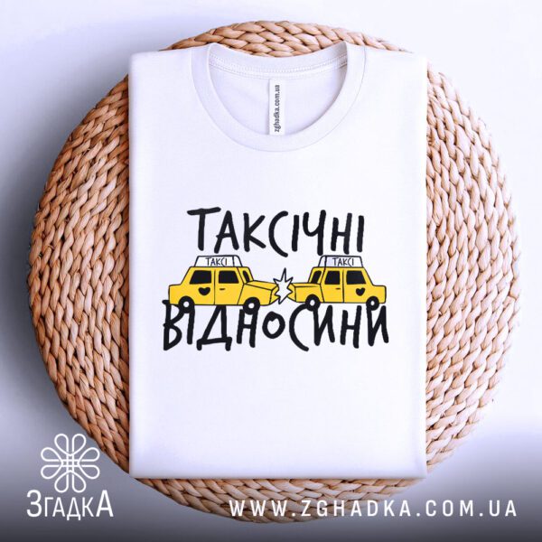 Біла футболка з принтом "таксічні відносини жарт", акуратно складена на круглій дерев'яній поверхні.