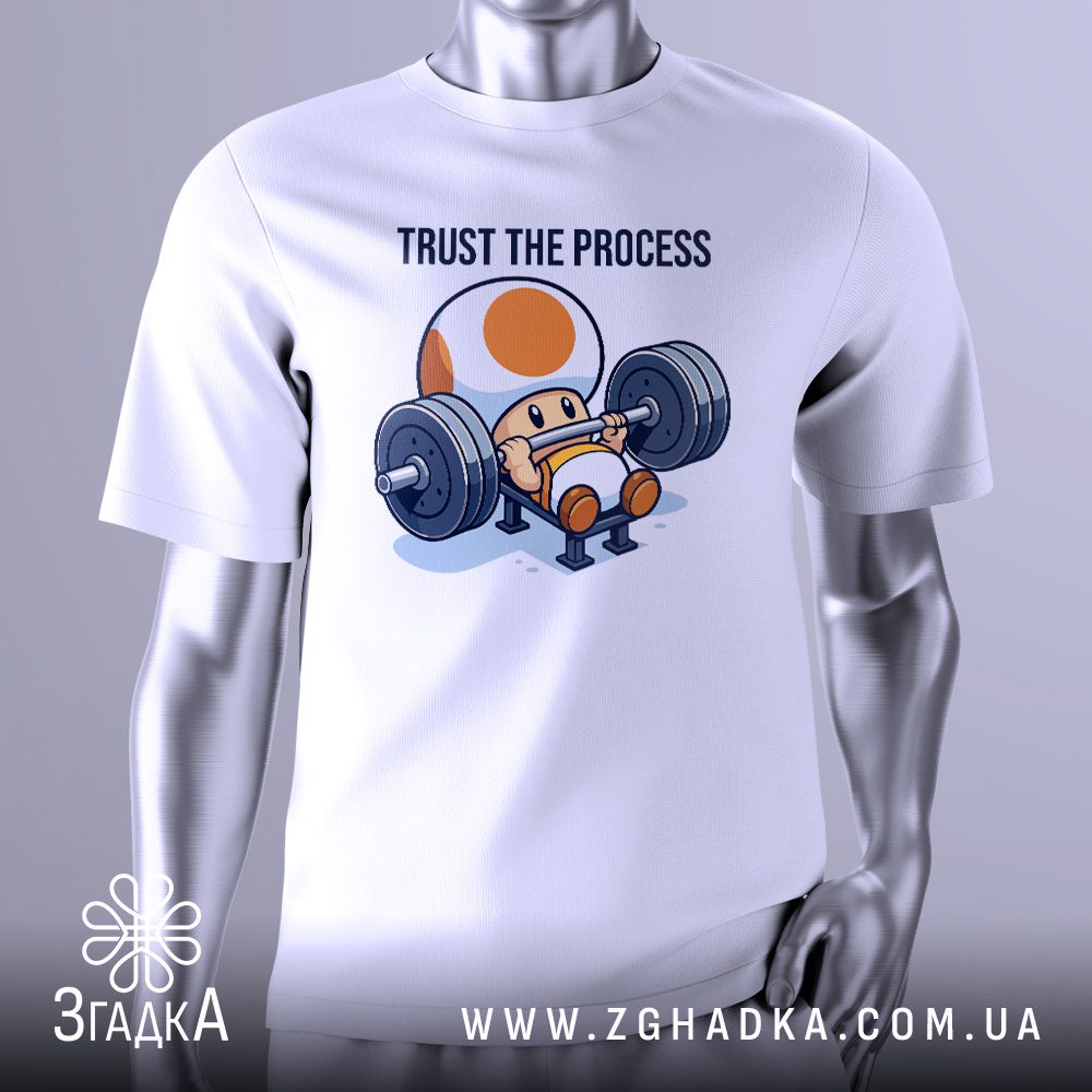 Біла футболка з чорним текстовим принтом "Trust the process". Напис виконаний простим, чітким шрифтом. Футболка представлена на сірому манекені.