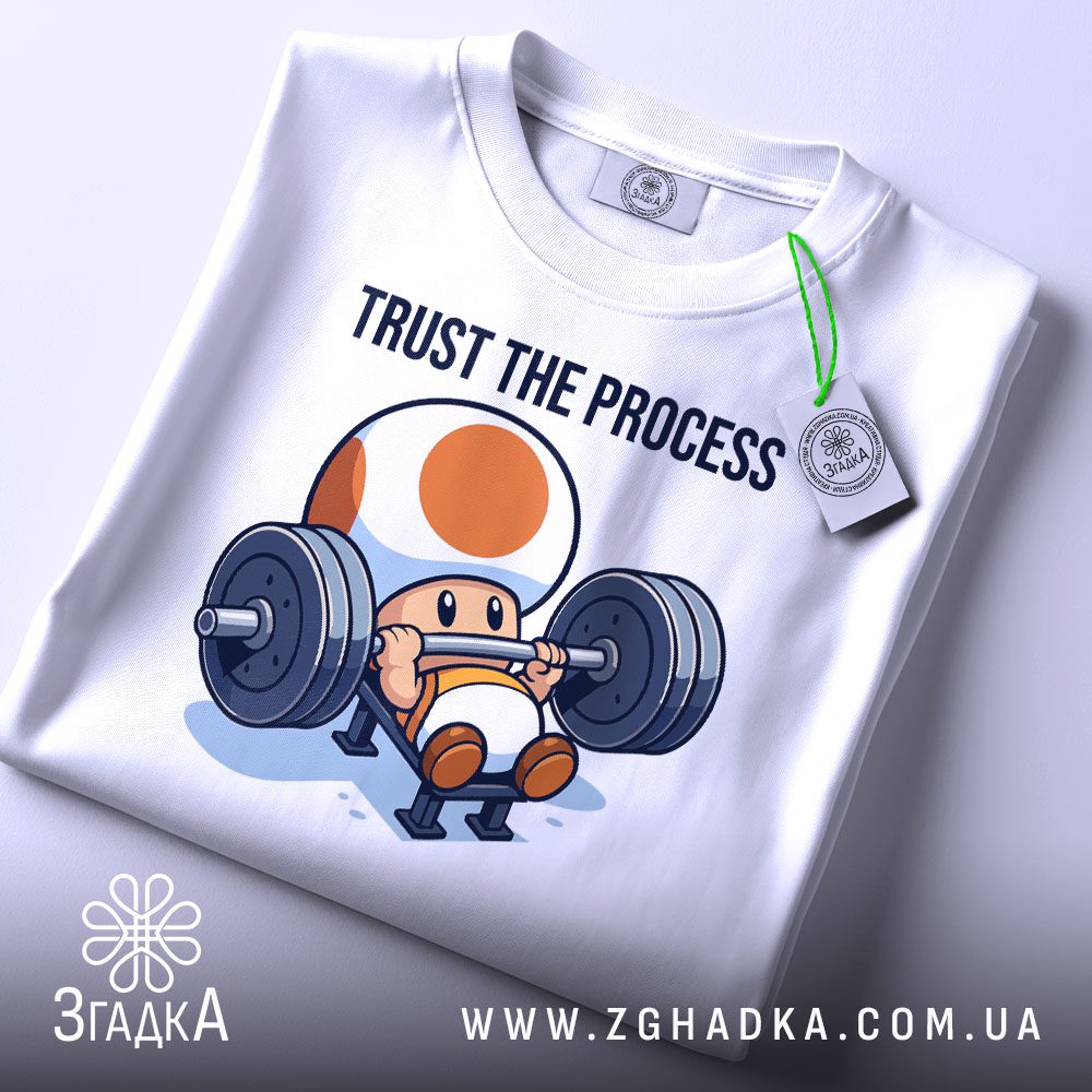 Складена біла футболка з чорним текстовим принтом "Trust the process" та етикеткою "Згадка".