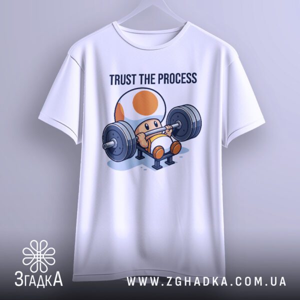 Біла футболка з принтом "Trust the process", що висить на білих плічках.