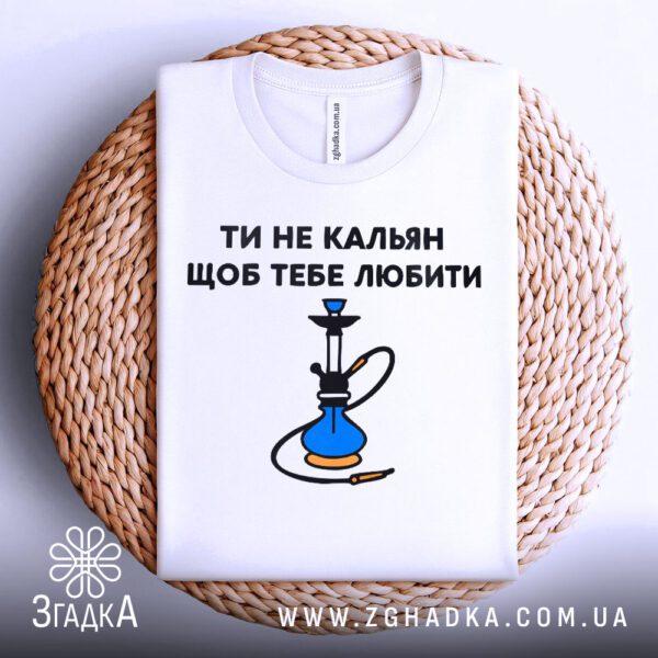 Біла футболка з принтом "ти не кальян", акуратно складена на круглій дерев'яній поверхні.
