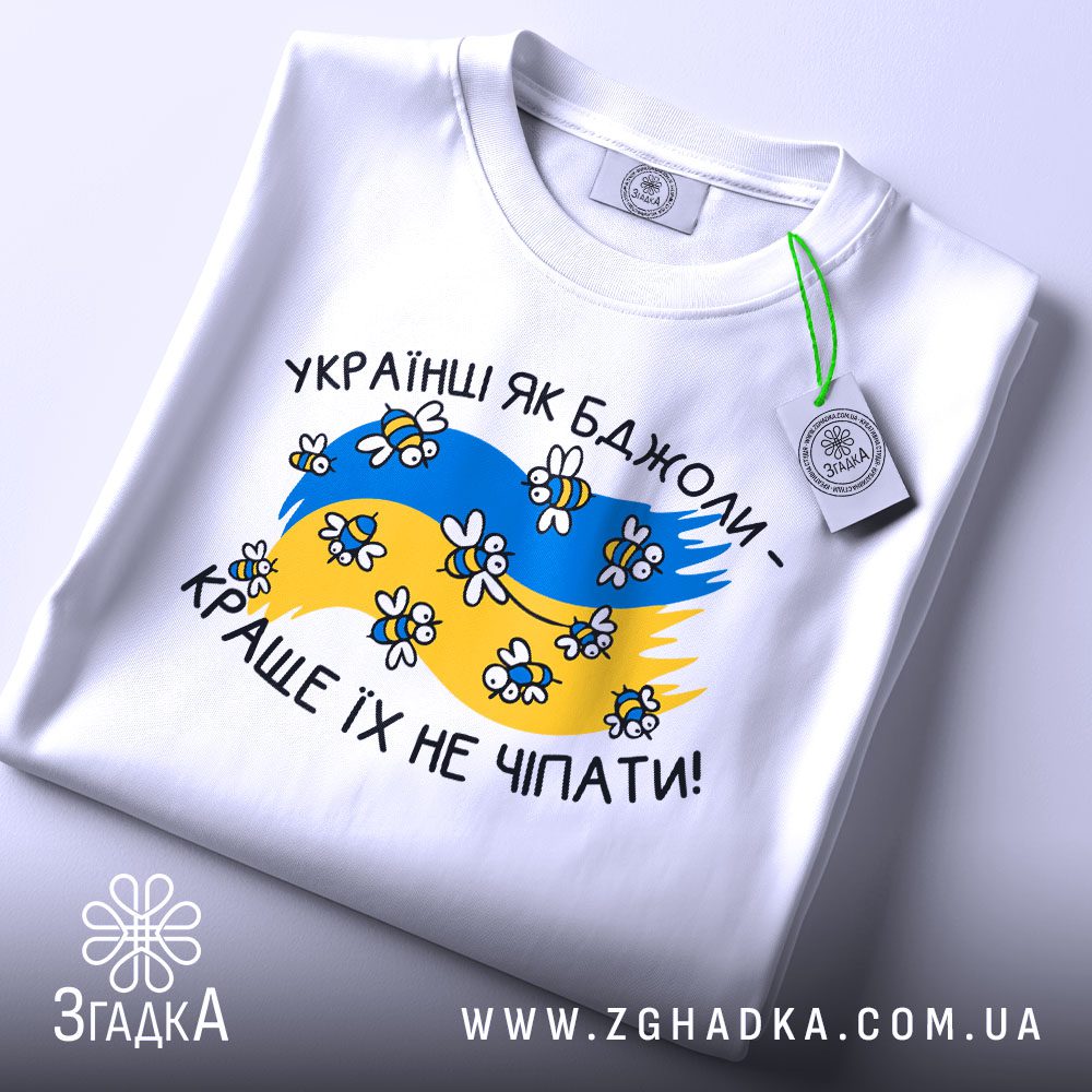 Складена біла футболка з принтом "Українці як бджоли" та етикеткою "Згадка".