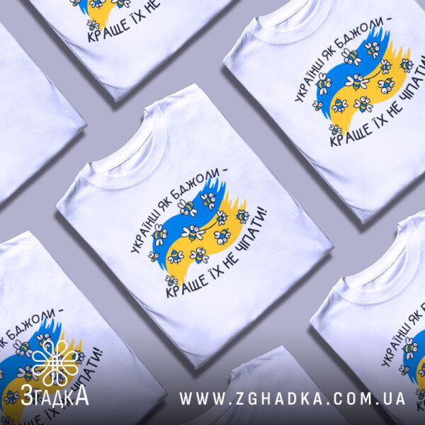 Кілька білих футболок з принтом "Українці як бджоли", складені стопкою або розкладені поруч на світлому фоні.