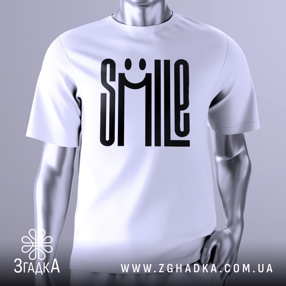 Біла футболка з великим чорним текстовим принтом у центрі. Напис "SMILE" виконаний таким чином, що літери "M" і "I" утворюють очі, а літера "L" – ніс, а вигнута лінія під ними – посмішку. Загалом принт нагадує усміхнене обличчя. Футболка на сірому манекені.
