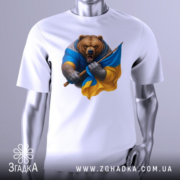 Біла футболка з графічним принтом у центрі. На принті зображений стилізований, розлючений ведмідь. Частина його тіла обгорнута прапором України (синьо-жовтим), а в лапі він тримає спис. Фон може бути темним або абстрактним, підкреслюючи фігуру ведмедя. Футболка на сірому манекені.