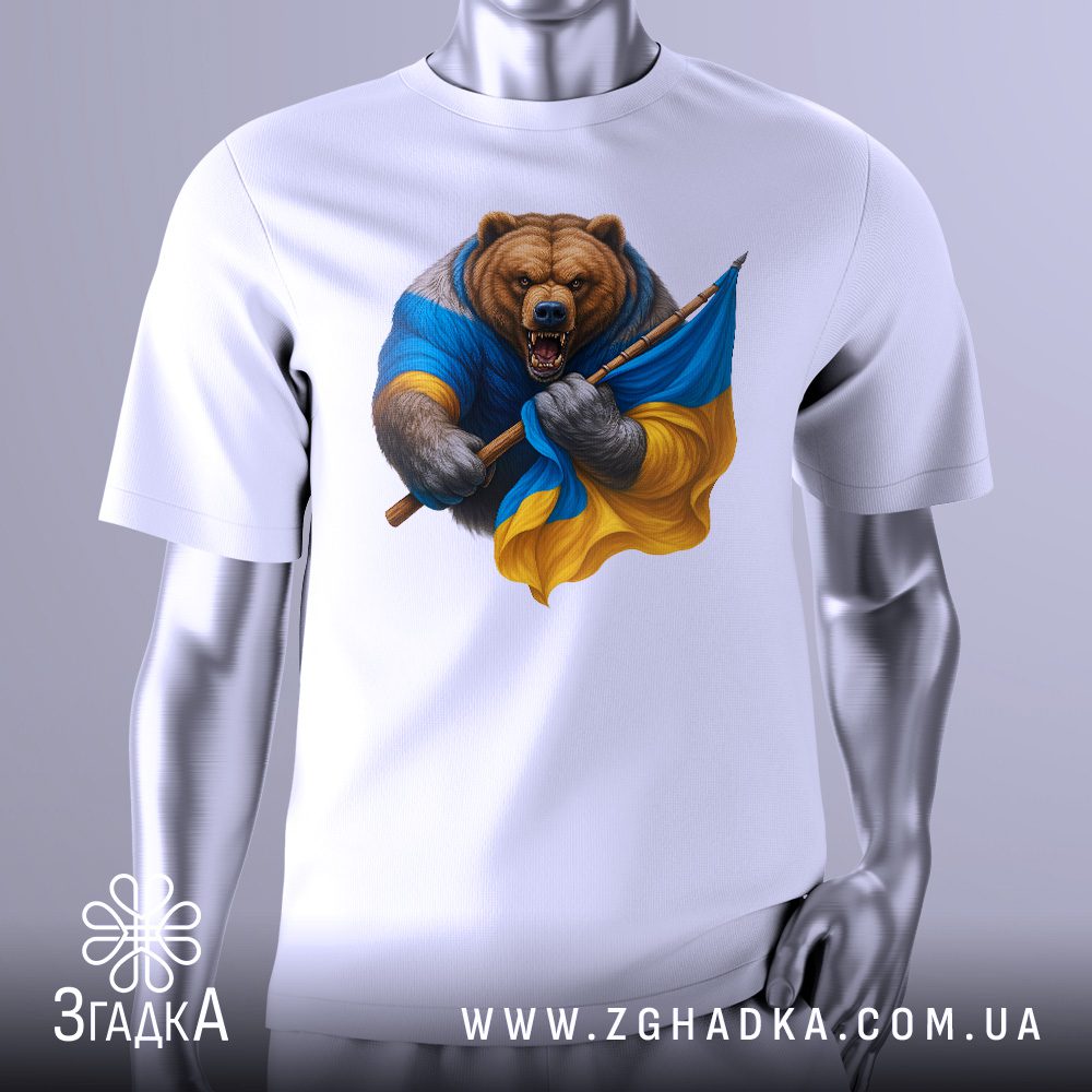 Біла футболка з графічним принтом у центрі. На принті зображений стилізований, розлючений ведмідь. Частина його тіла обгорнута прапором України (синьо-жовтим), а в лапі він тримає спис. Фон може бути темним або абстрактним, підкреслюючи фігуру ведмедя. Футболка на сірому манекені.