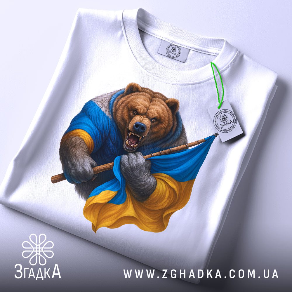Складена біла футболка з принтом "ведмідь з прапором" та етикеткою "Згадка".
