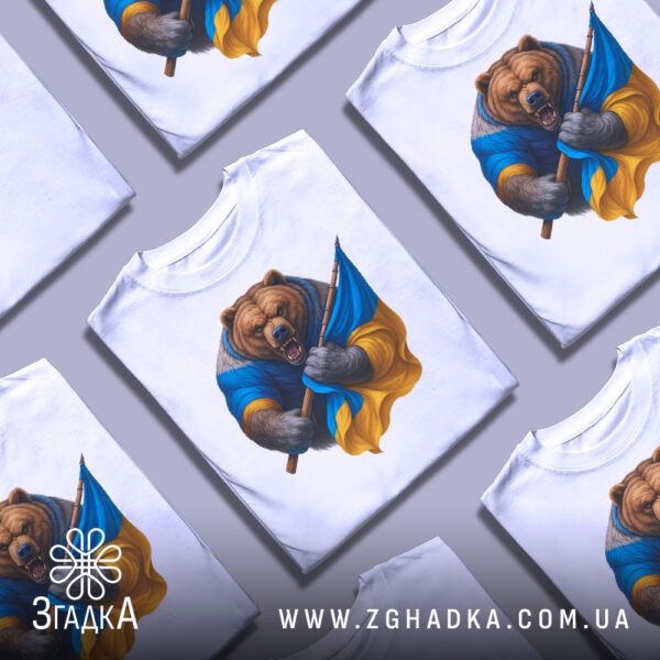 Кілька білих футболок з принтом "ведмідь з прапором", складені стопкою або розкладені поруч на світлому фоні.