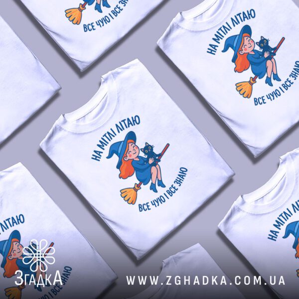 Кілька білих футболок з принтом відьмочки на мітлі, складені одна на одну або розкладені поруч на сірому фоні.
