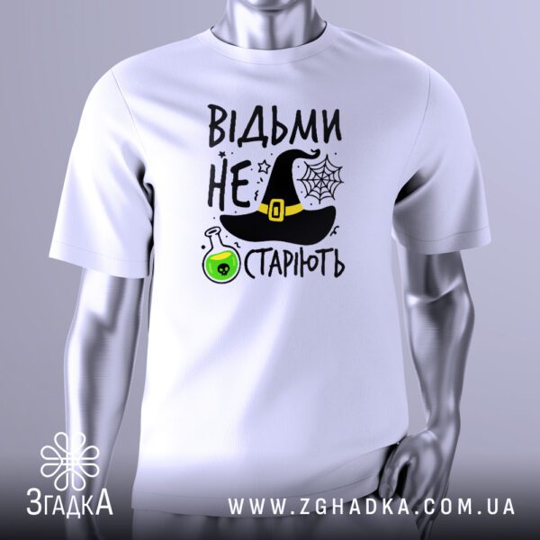Біла футболка з кольоровим принтом у центрі. Напис "Відьми не старіють" виконаний стилізованим шрифтом. Над написом розташований чорний відьомський капелюх, а поруч — зелена колба з бульбашками. Фон прикрашений елементами павутиння та невеликими зірками. Футболка на сірому манекені.