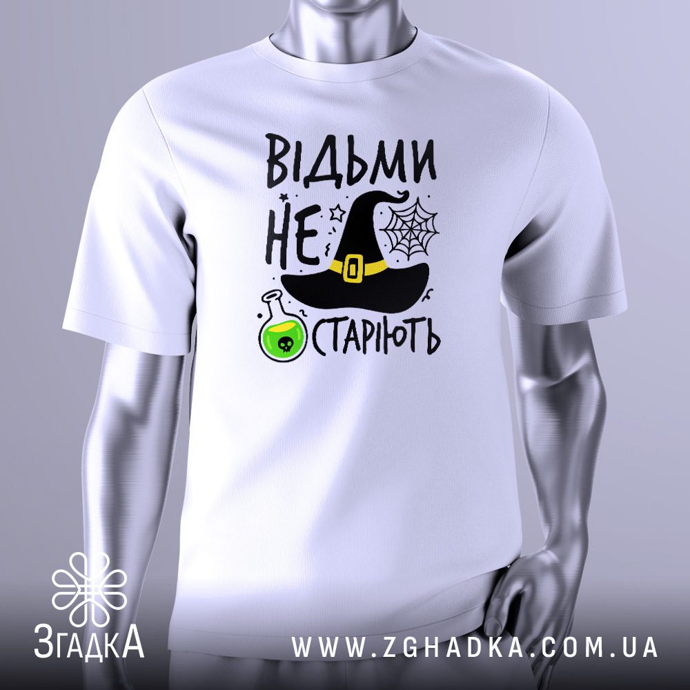 Біла футболка з кольоровим принтом у центрі. Напис "Відьми не старіють" виконаний стилізованим шрифтом. Над написом розташований чорний відьомський капелюх, а поруч — зелена колба з бульбашками. Фон прикрашений елементами павутиння та невеликими зірками. Футболка на сірому манекені.