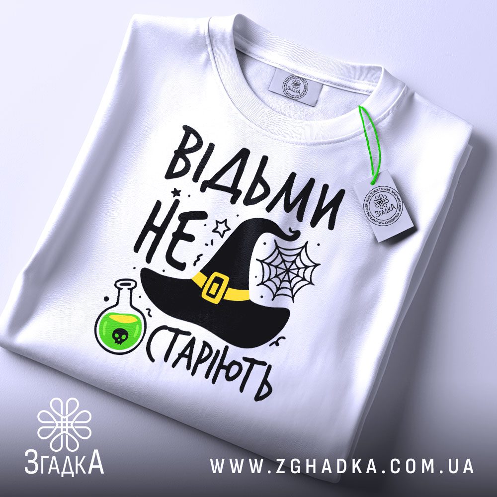 Складена біла футболка з принтом "відьми не старіють" та етикеткою "Згадка".