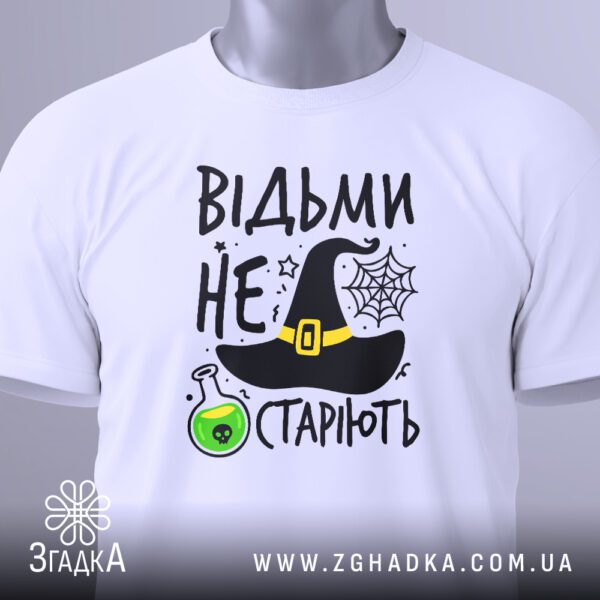 Крупний план принта "Відьми не старіють" на білій футболці, що детально показує елементи дизайну: капелюх, колбу, павутиння.