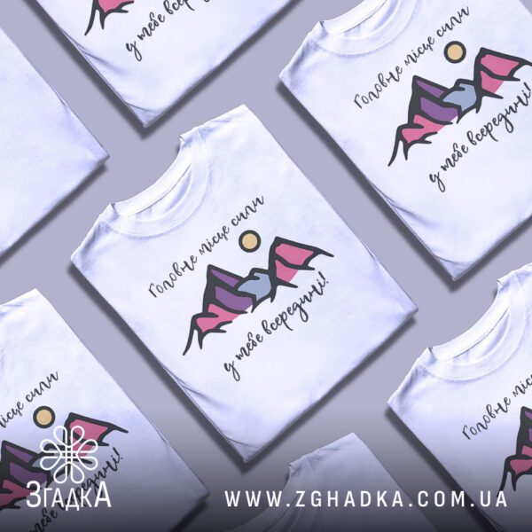 Кілька білих футболок з принтом "внутрішня сила людини", складені стопкою або розкладені поруч на світлому фоні.
