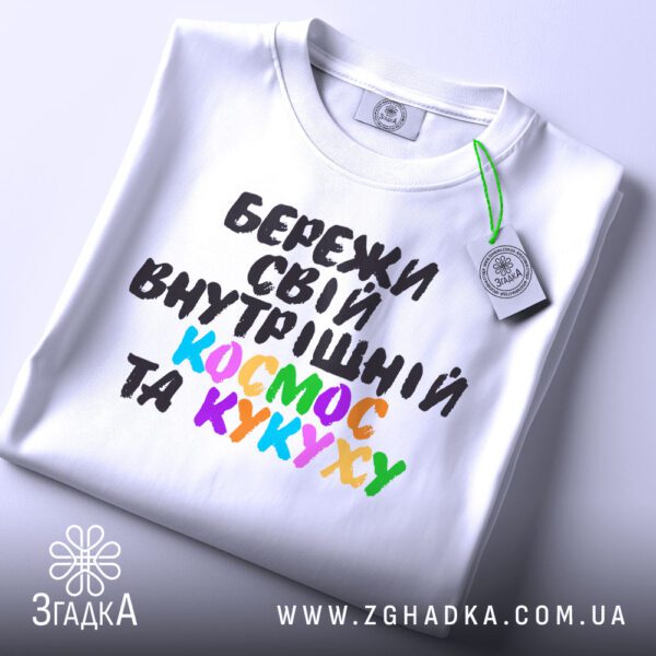 Складена біла футболка з принтом "всередині цілий всесвіт" та етикеткою "Згадка".