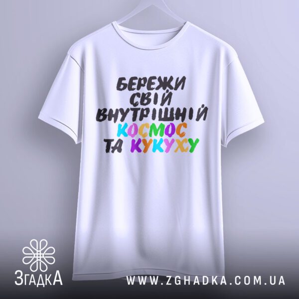 Біла футболка з принтом "всередині цілий всесвіт", що висить на білих плічках, демонструючи дизайн.