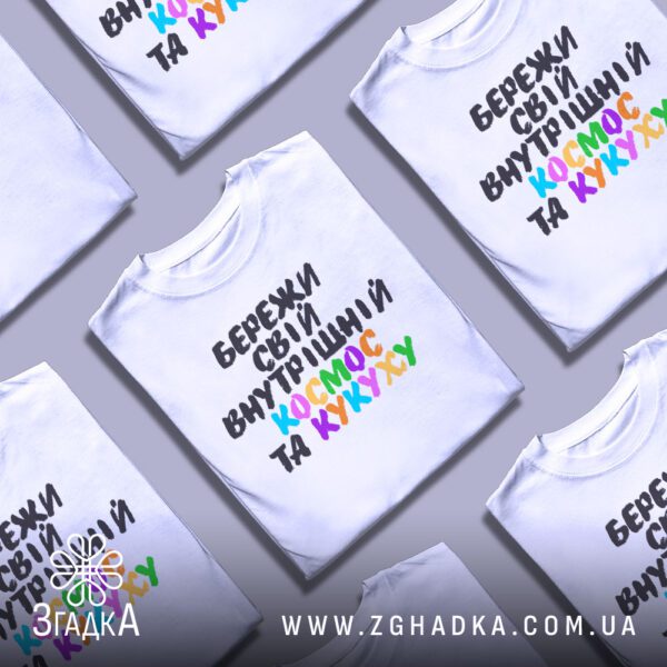 Кілька білих футболок з принтом "всередині цілий всесвіт", складені стопкою або розкладені поруч на світлому фоні.