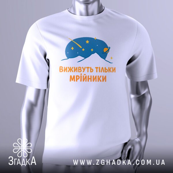 Біла футболка з графічним принтом у центрі. На принті зображено абстрактну, футуристичну істоту або об'єкт у космічному стилі, з текстурою, що нагадує галактику чи зорі. Над нею напис "Виживуть тільки мрійники". Футболка на сірому манекені.
