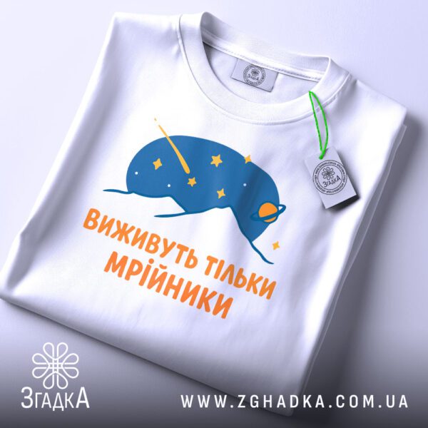 Складена біла футболка з принтом "виживуть тільки мрійники" та етикеткою "Згадка".