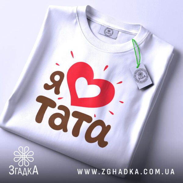 Складена біла футболка з принтом "Я ♥ тата" та етикеткою "Згадка".
