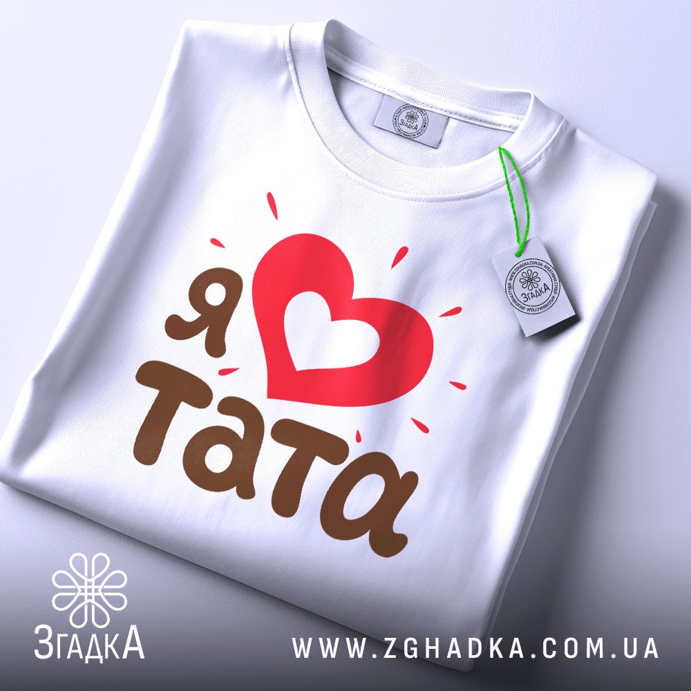 Складена біла футболка з принтом "Я ♥ тата" та етикеткою "Згадка".
