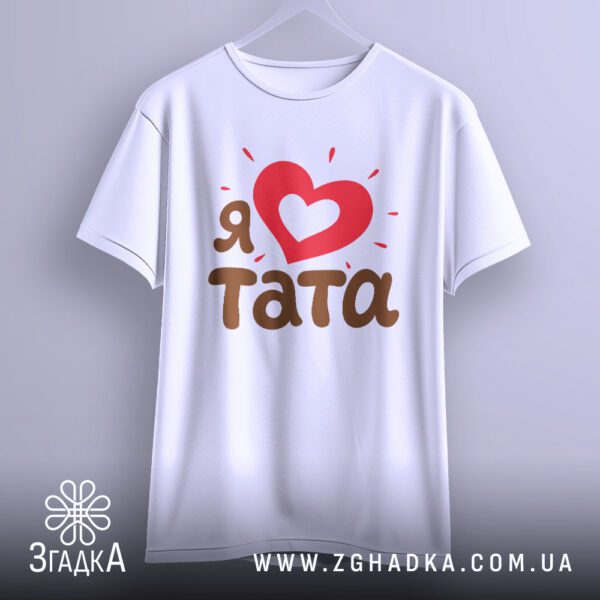 Біла футболка з принтом "Я ♥ тата", що висить на білих плічках, демонструючи дизайн.