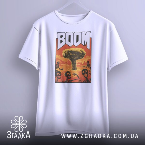 Біла футболка з принтом "ядерний вибух BOOM", що висить на білих плічках, демонструючи дизайн.