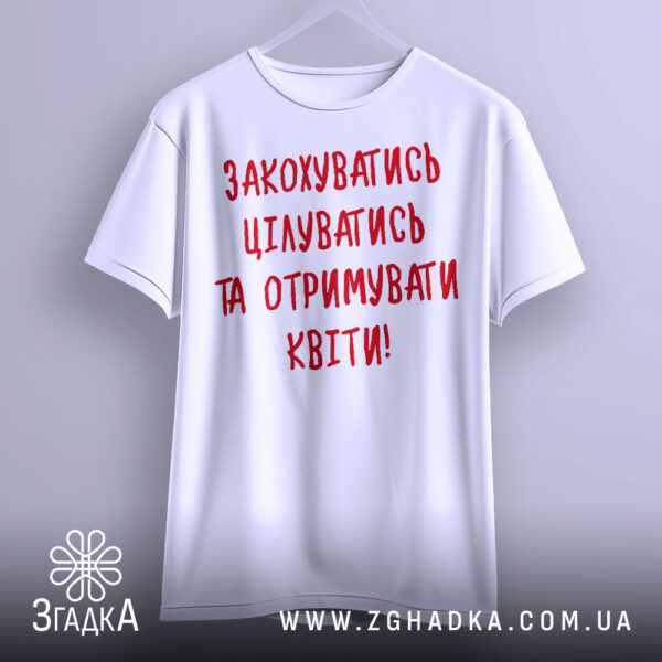 Біла футболка з принтом "любовний посил", що висить на білих плічках, демонструючи дизайн.