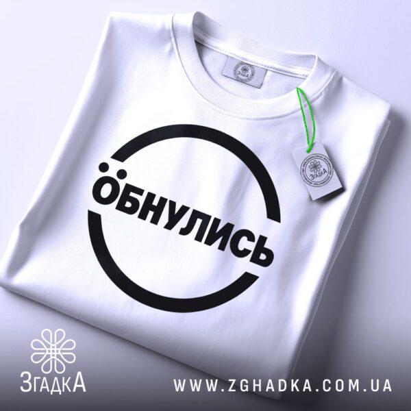 Складена біла футболка з принтом "Обнулись" та етикеткою "Згадка".