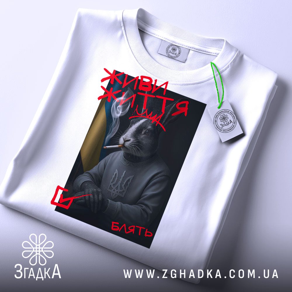 Складена біла футболка з принтом "живи життя кролик" та етикеткою "Згадка".