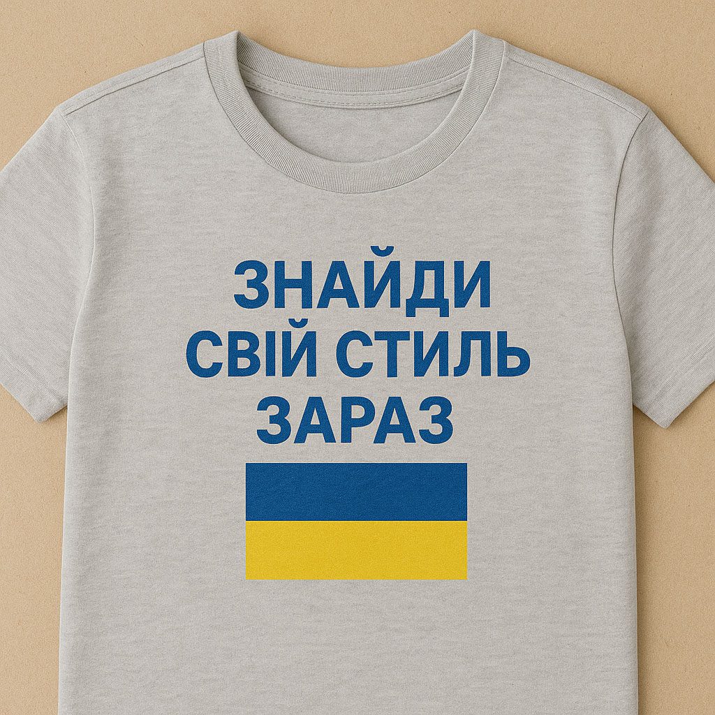 Сіра патріотична футболка з написом "ЗНАЙДИ СВІЙ СТИЛЬ ЗАРАЗ" синім кольором і зображенням українського прапора на фоні бежевого тла.