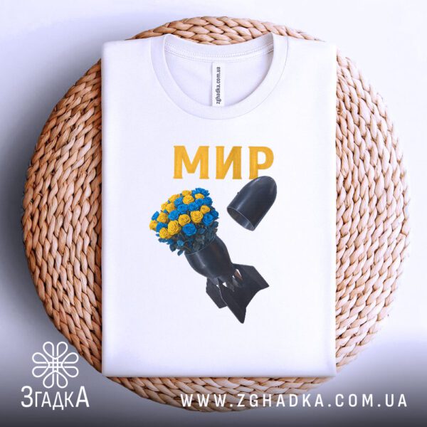 Біла футболка з антивоєнним принтом, що висить на вішаку.