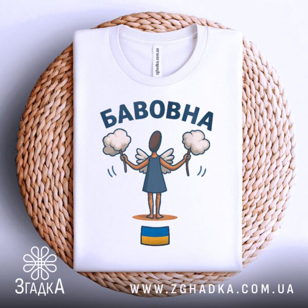 Біла футболка з принтом "бавовна з прапором", акуратно складена на круглій дерев'яній поверхні.