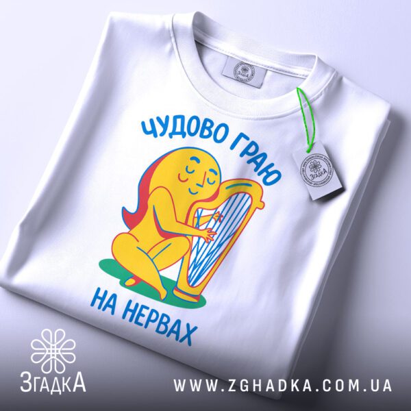 Складена біла футболка з принтом "чудово граю на нервах" та етикеткою "Згадка".