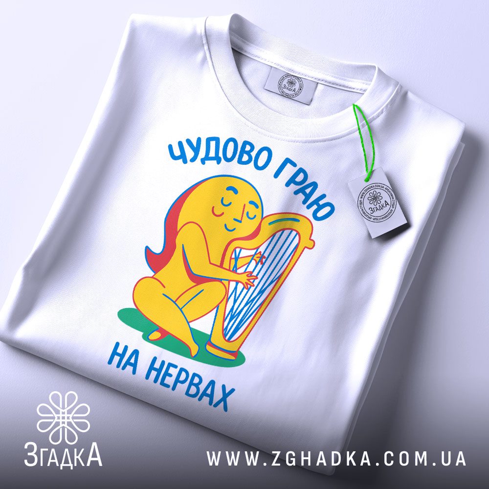 Складена біла футболка з принтом "чудово граю на нервах" та етикеткою "Згадка".