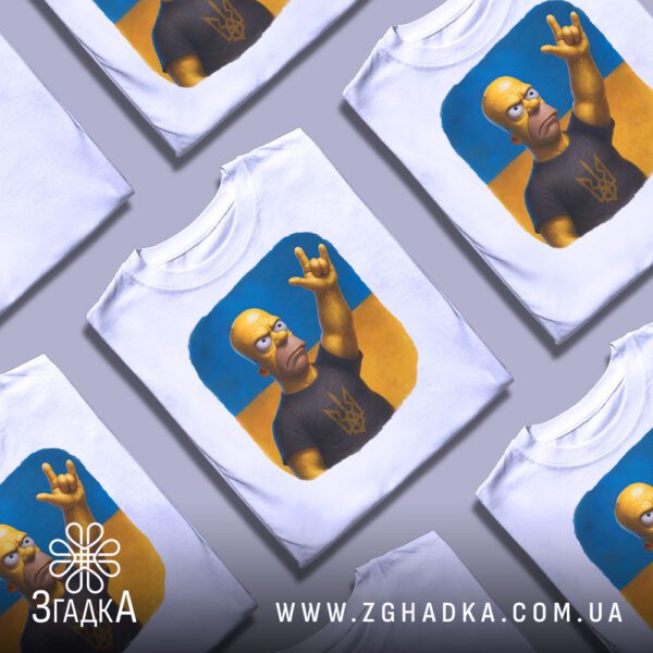 Кілька білих футболок з принтом "Гомер Сімпсон патріот", складені стопкою або розкладені поруч на світлому фоні.