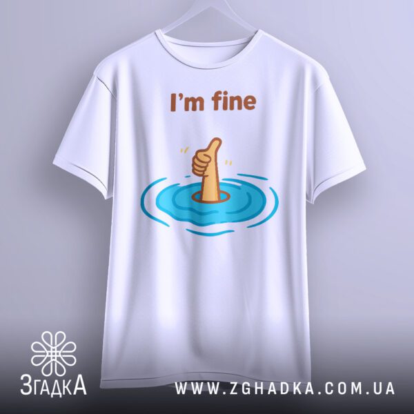 Біла футболка з принтом "I'm fine гумор", що висить на білих плічках, демонструючи дизайн.