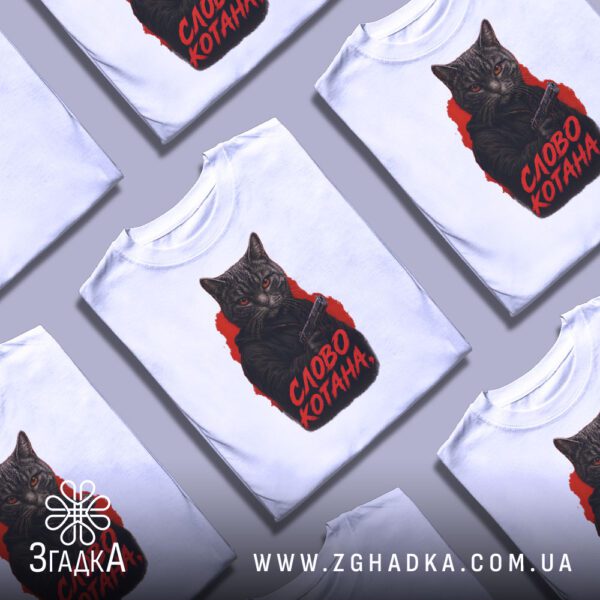 Біла футболка з принтом «котан з пістолетом», складена на поверхні.