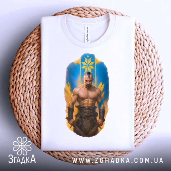 Біла футболка з принтом "козацька сила Україна", акуратно складена на круглій дерев'яній поверхні.